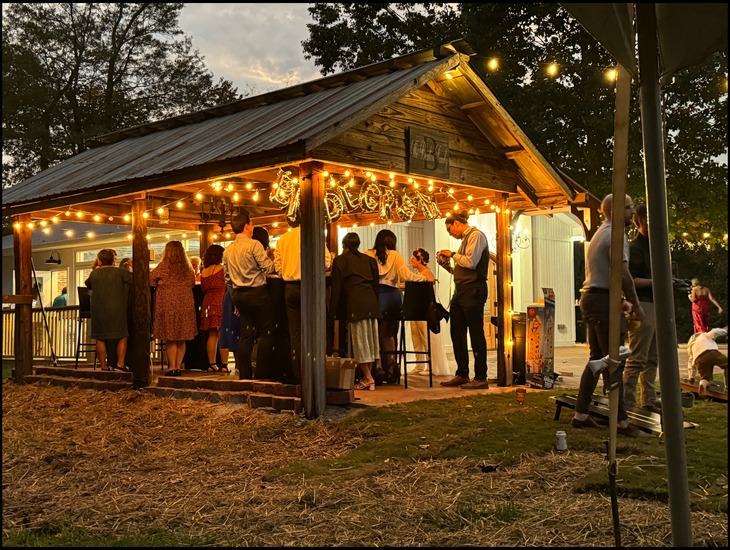 The pavilion lit with string lights at night with guests gathered on the brick courtyard