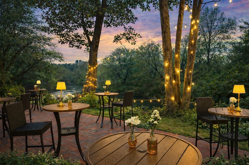 Covered deck with bistro tables and lantern lighting overlooking the river at dusk