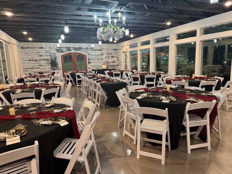 Event hall set with round tables and white chairs facing a wall of glass over the river